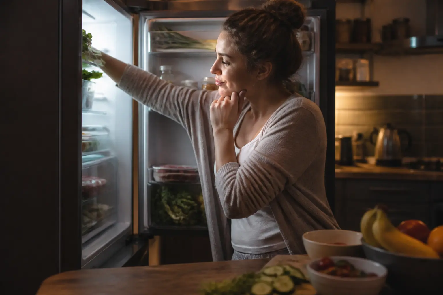 Femme dans une cuisine moderne, devant un frigo ouvert la nuit, illustrant pourquoi j ai tout le temps faim et grignote souvent